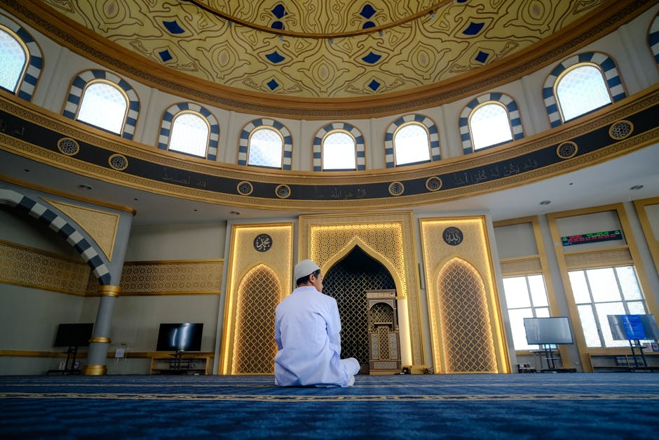 A man in traditional clothing prays inside a stunning mosque interior, embracing spiritual peace.
